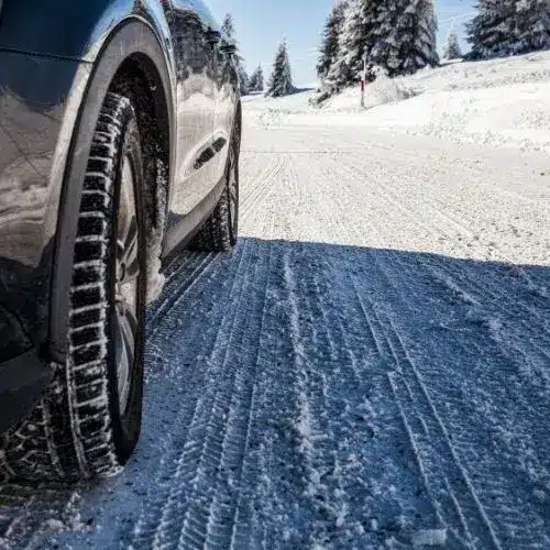 Four car tires displayed in a gradient setting, transitioning from a sunny environment to a snowy road, highlighting summer and winter tire tread patterns for optimal performance in varying weather conditions.