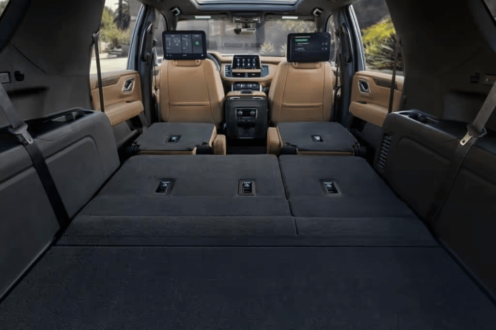 Interior view of a spacious SUV with the rear seats folded down, showcasing ample cargo space and modern technology features, including dual display screens on the front seats and a sleek dashboard design.