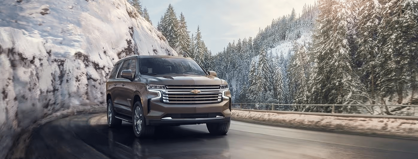 A Chevrolet SUV driving on a snow-covered road, surrounded by pine trees and mountains, showcasing winter driving capability and premium design.