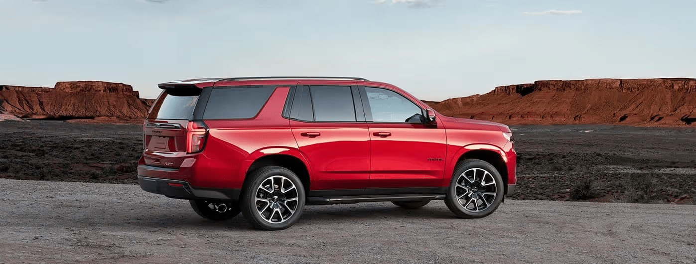 Red SUV parked on rocky terrain with a desert landscape and distant cliffs in the background, showcasing its sleek design and modern features.