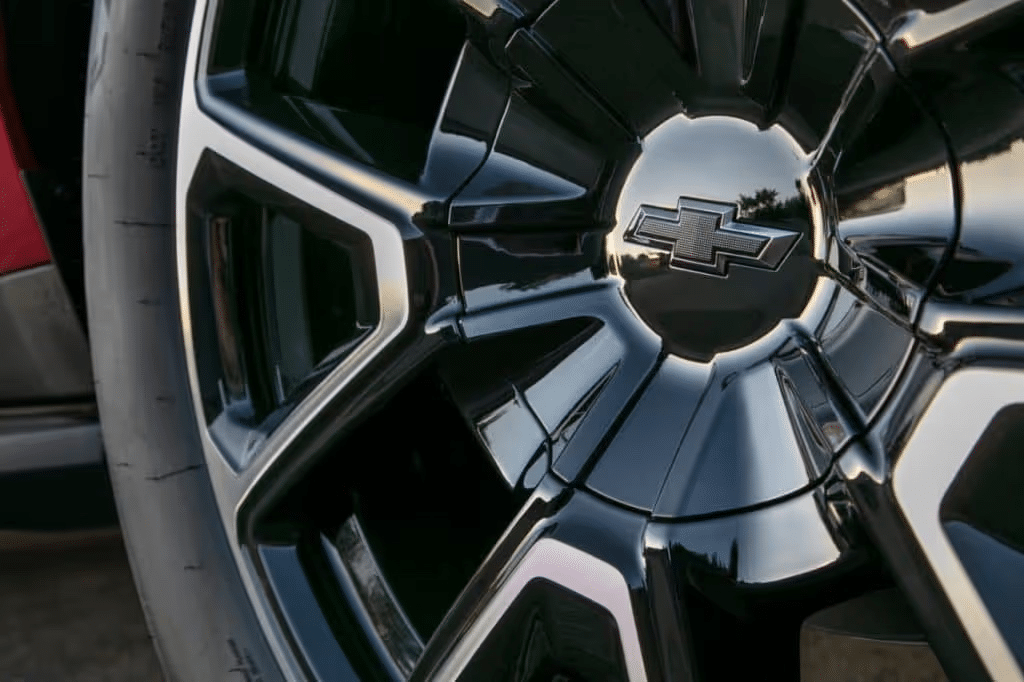 Close-up view of a black Chevrolet wheel rim featuring the iconic bowtie logo, showcasing its sleek design and glossy finish against a blurred background.