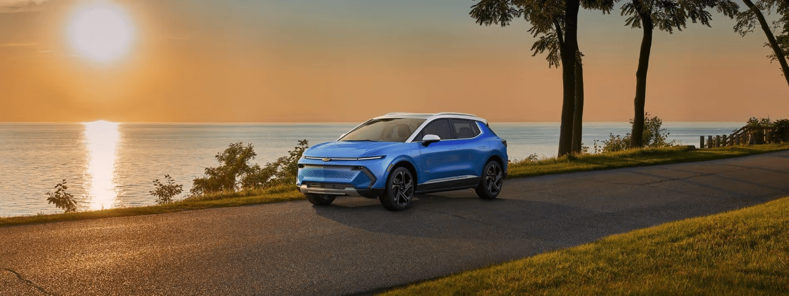 A Chevrolet SUV driving on a gravel road surrounded by lush greenery and trees under a clear blue sky, showcasing its off-road capabilities and exterior design.