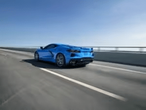 Blue sports car driving on an open highway under a clear sky, showcasing its sleek design and powerful rear profile.