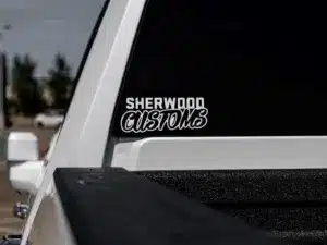 White truck with a black rear window displaying a custom decal reading "Sherwood Customs," set against an outdoor parking lot backdrop.