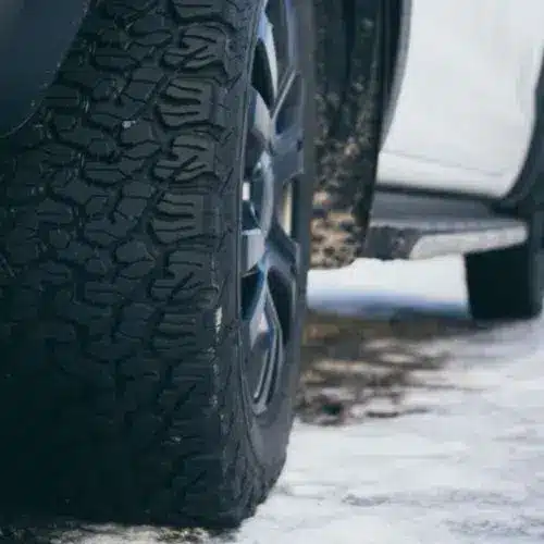 Four car tires displayed in a gradient setting, transitioning from a sunny environment to a snowy road, highlighting summer and winter tire tread patterns for optimal performance in varying weather conditions.