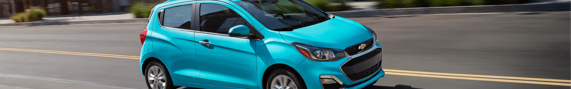 Vibrant blue Chevrolet Spark compact car driving on a city street, showcasing its sporty design and agility.