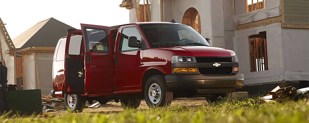 Red Chevrolet van parked at a construction site with open doors, surrounded by building materials and structures in progress. Ideal for work and transportation needs.