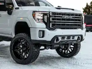 GMC truck with a bold front grille, featuring aftermarket black alloy wheels, parked in a snowy environment, showcasing its rugged design and off-road capabilities.
