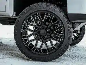 Close-up of a black forged wheel with aggressive tread tires, mounted on a pickup truck, showcasing a rugged design ideal for off-road adventures and winter driving conditions.