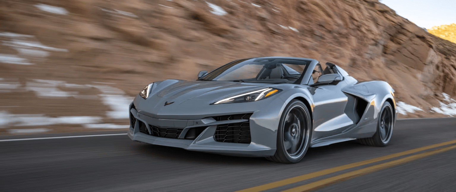 High-performance silver sports car driving on a winding mountain road, showcasing aerodynamic design and modern features against a rocky backdrop.