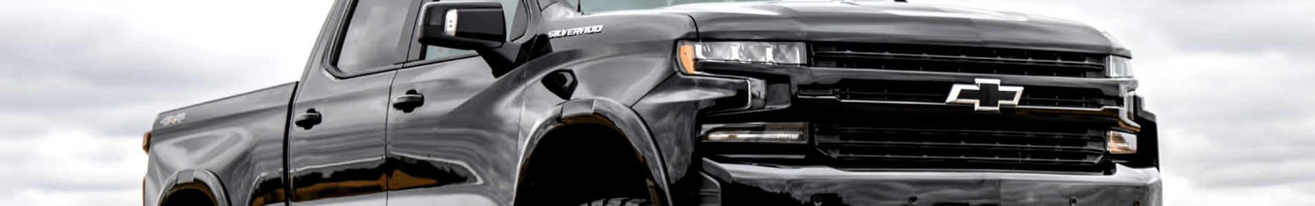 Black Chevrolet Silverado truck showcasing its front design and aggressive stance against a cloudy background. Ideal for rugged terrains and durability. Perfect for work and outdoor adventures.