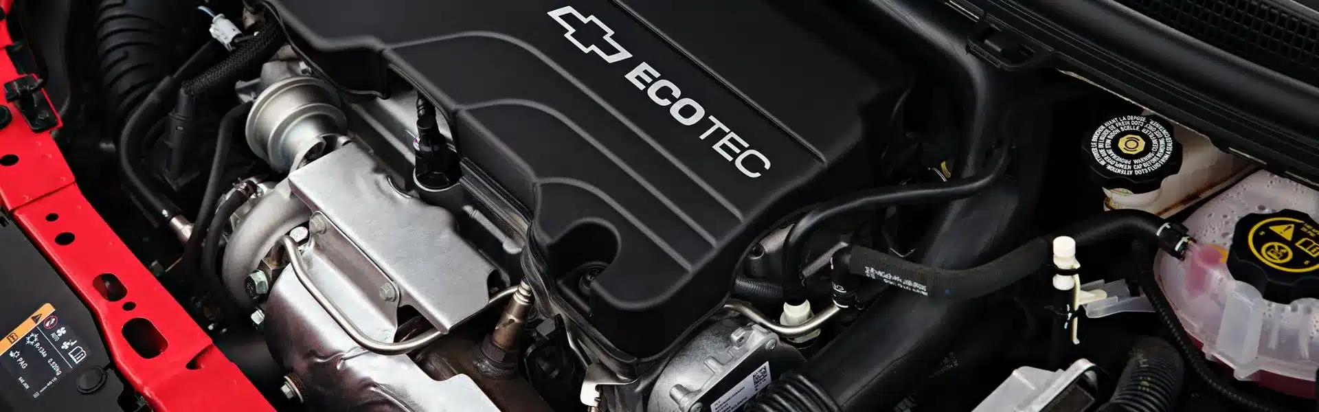 Close-up view of a Chevrolet Ecotec engine, showcasing the engine cover with the Ecotec logo, various engine components, and surrounding parts in an automotive setting.