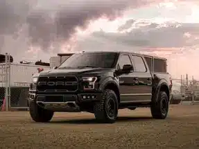 Black Ford F-150 Raptor parked in an industrial setting, showcasing its rugged design and off-road capabilities against a dramatic sky.