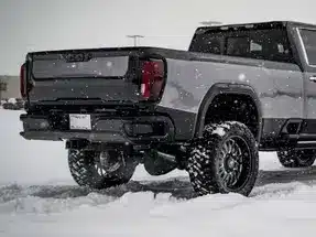 Gray pickup truck with oversized tires parked in snowy conditions, showcasing its off-road capabilities and rugged design.