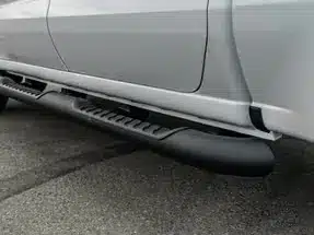 Close-up view of a black running board installed on the side of a silver pickup truck, showcasing its textured surface and functional design.
