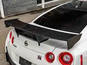 Close-up of the rear of a white Nissan GT-R showcasing a prominent black rear wing, highlighting its sleek design and performance features.
