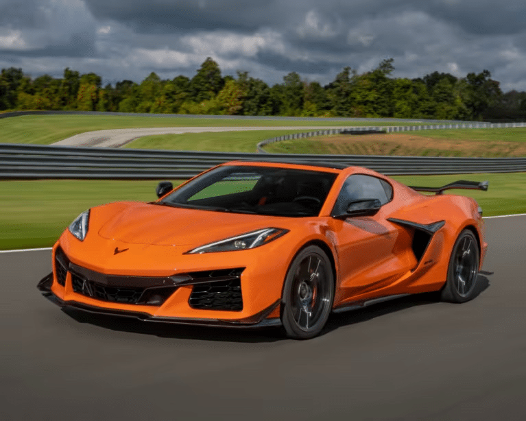 Orange Chevrolet Corvette C8 Z06 sports car speeding on a racetrack, showcasing its sleek design and aerodynamic features against a green landscape and cloudy sky.