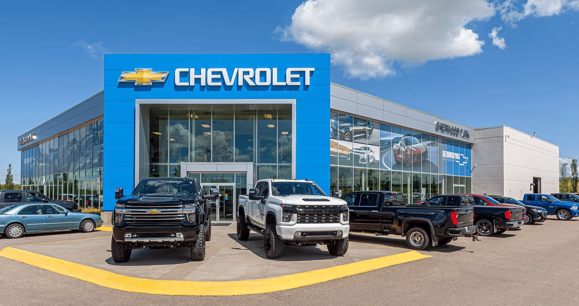 Chevrolet dealership exterior with multiple trucks on display, showcasing a modern design and bright blue branding. The location features large glass windows for visibility and a diverse selection of vehicles in the lot under a clear blue sky.