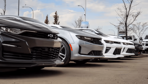 Lineup of sporty cars, showcasing modern designs, including black and white models parked in a dealership setting under a clear sky.