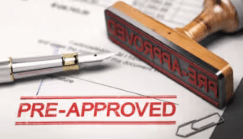 Close-up of a "Pre-Approved" stamp on financial documents, alongside a fountain pen and paper clips, illustrating loan approval or credit pre-qualification process.