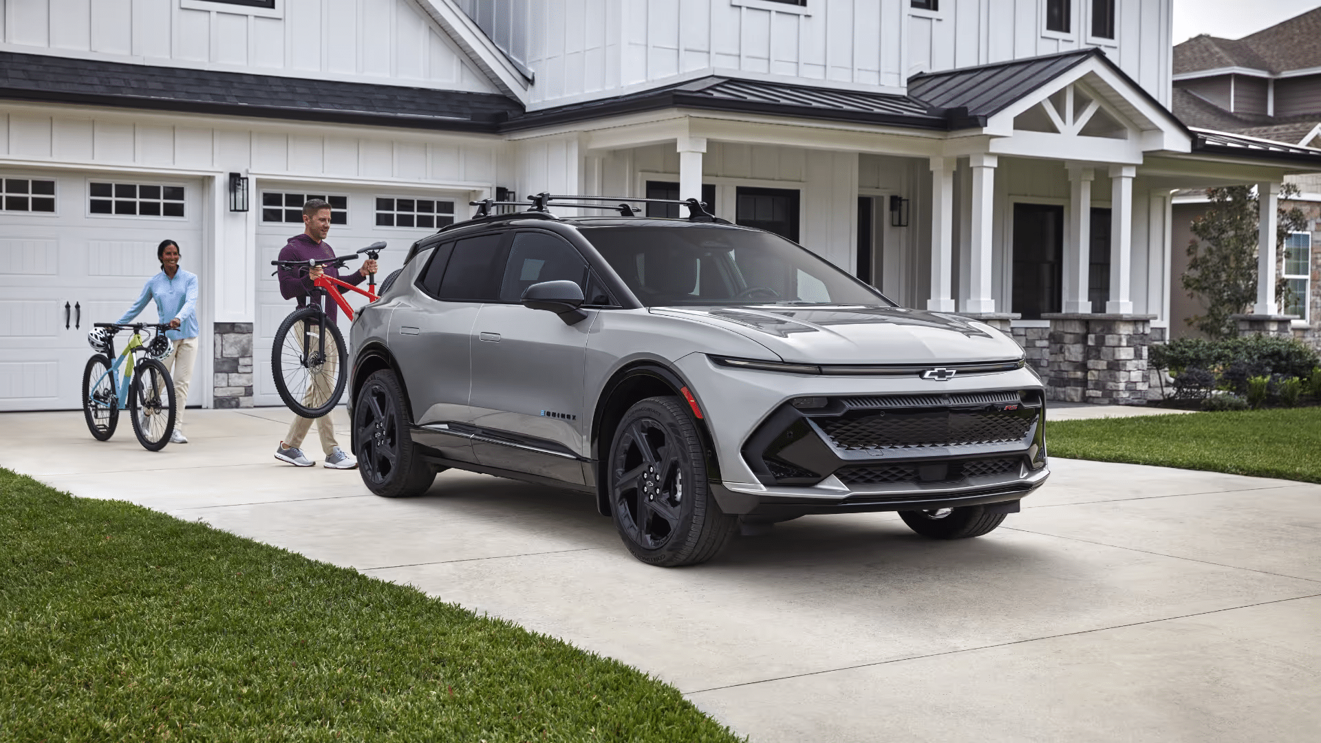 Couple loading mountain bikes onto a new Chevrolet Equinox parked in front of a modern home, showcasing outdoor lifestyle and adventure readiness.