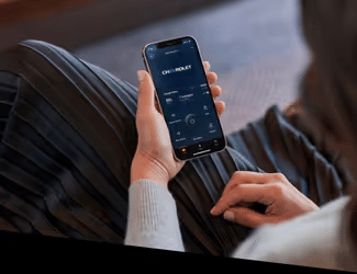 Person using a smartphone to interact with a mobile app interface, showcasing features for managing finances or investments, while sitting comfortably in a cozy setting.