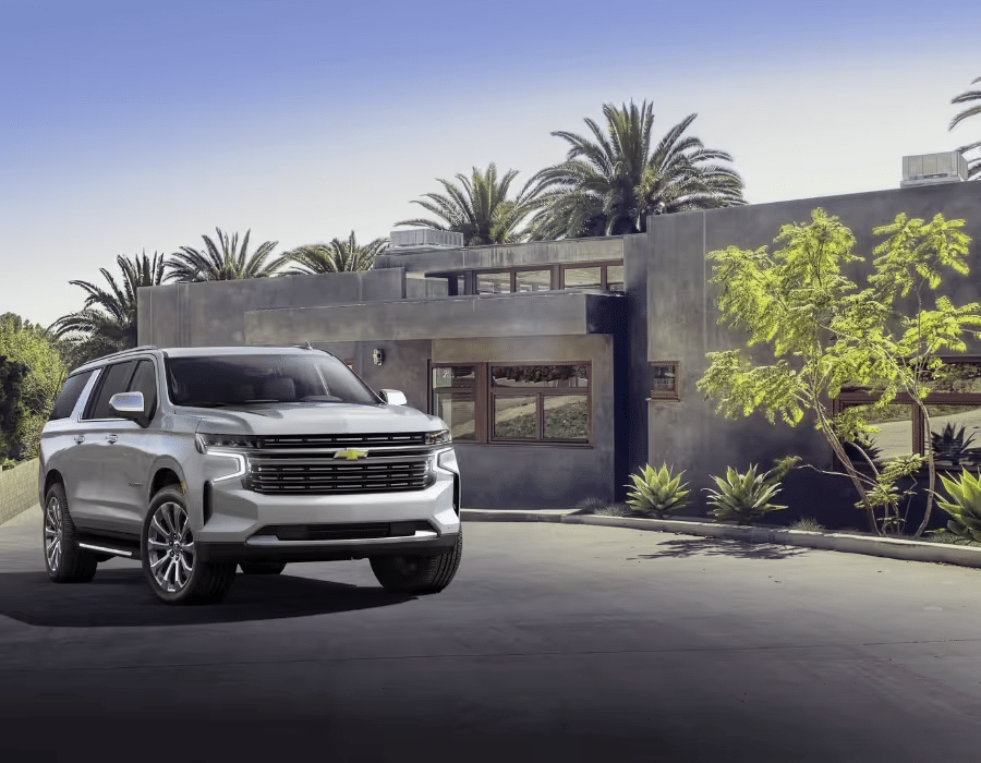 A silver Chevrolet SUV parked in front of a modern house with palm trees and greenery, showcasing luxury and style in an outdoor setting.