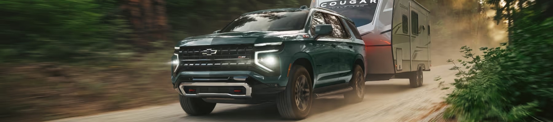 Chevrolet SUV towing a travel trailer on a dusty forest road, showcasing rugged performance and outdoor adventure capabilities.