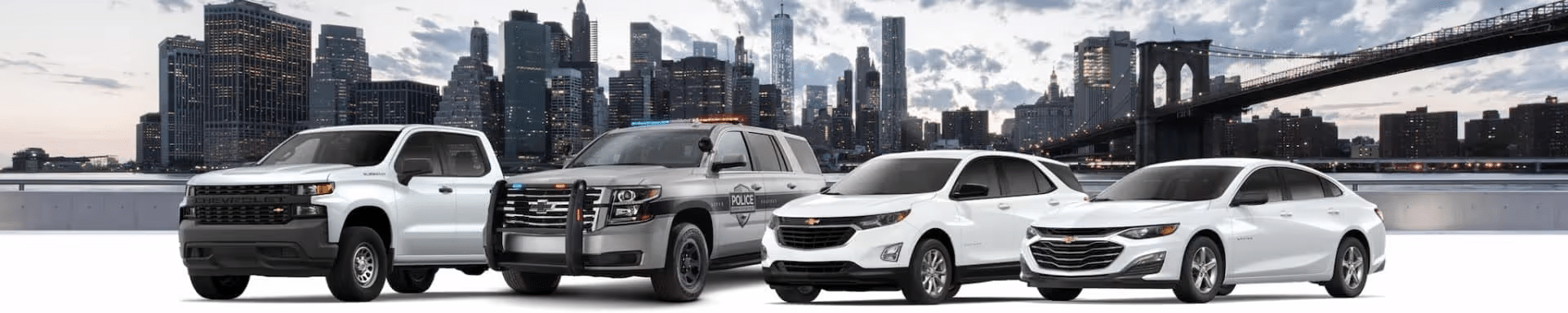 A lineup of various Chevrolet vehicles, including a pickup truck, police SUV, compact SUV, and sedan, set against a city skyline background. The image showcases the versatility and range of Chevrolet cars suitable for different driving needs.