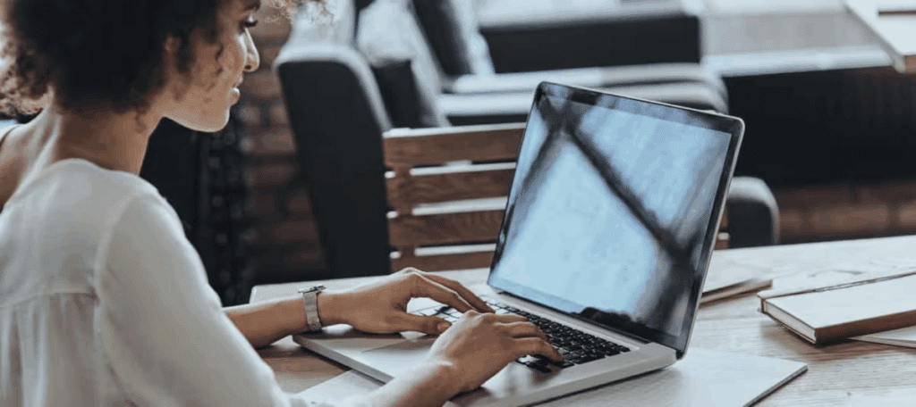 Woman working on a laptop in a stylish, modern workspace, focusing on her tasks with natural light illuminating the scene.