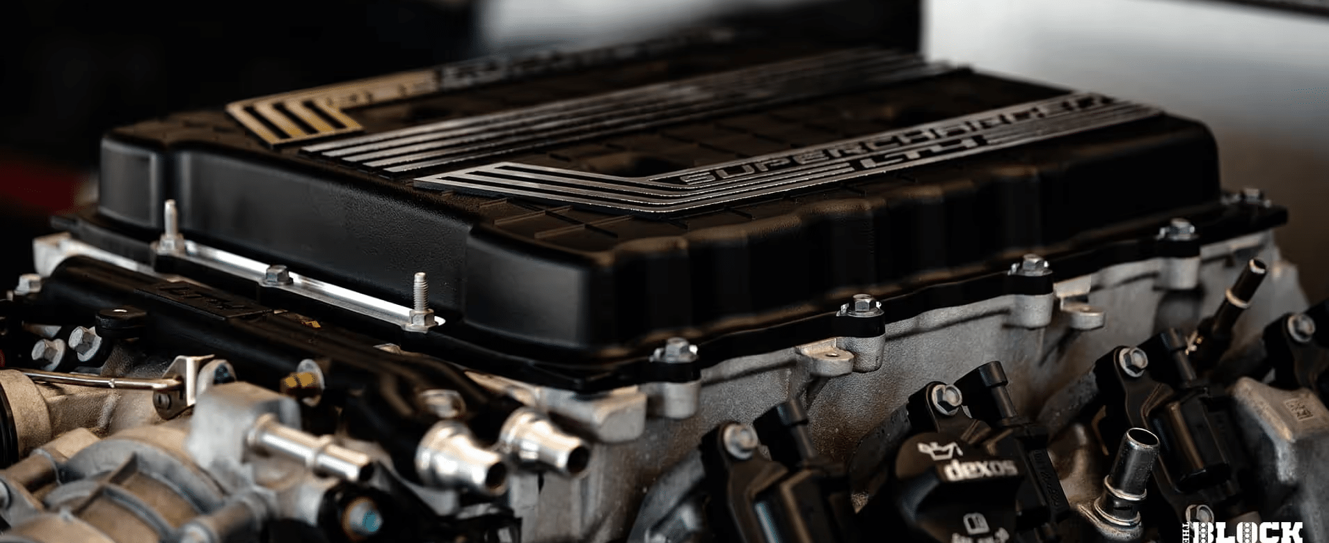 Close-up view of a high-performance engine with a supercharger, showcasing intricate details like the air intake system and engine components, highlighting automotive engineering and performance tuning.