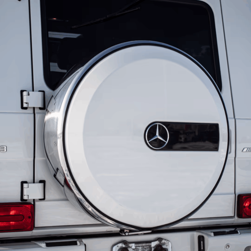Rear view of a white Mercedes-Benz G-Class SUV showcasing the iconic spare tire cover with the Mercedes logo. The photo highlights the vehicle's luxury design and distinctive features.