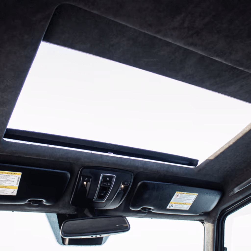 Interior view of a vehicle's sunroof with controls and overhead lights visible, showcasing a modern design and spacious feel.