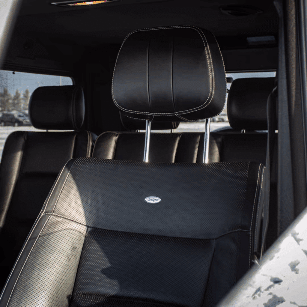 Interior view of a luxury car showcasing a black leather seat with perforated design and white stitching, featuring a prominent headrest, highlighting comfort and style.