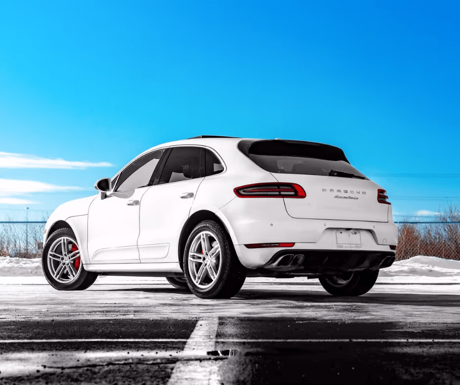 White Porsche Macan parked in a snowy environment under a clear blue sky, showcasing its sleek design and sport wheels.