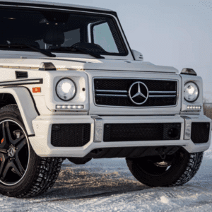 Mercedes-Benz G-Class SUV parked on snowy terrain, showcasing a sleek white exterior and distinctive front grille with LED headlights.