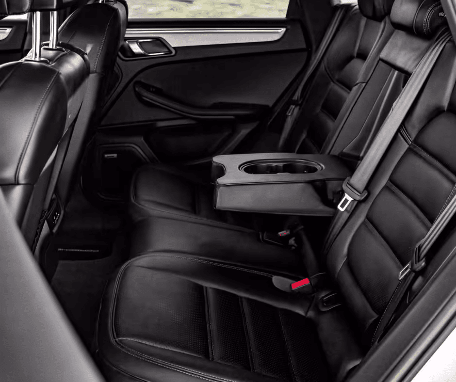 Luxury car interior showcasing black leather back seats with plush cushioning and integrated armrest featuring cup holders, designed for comfort and style during travel.