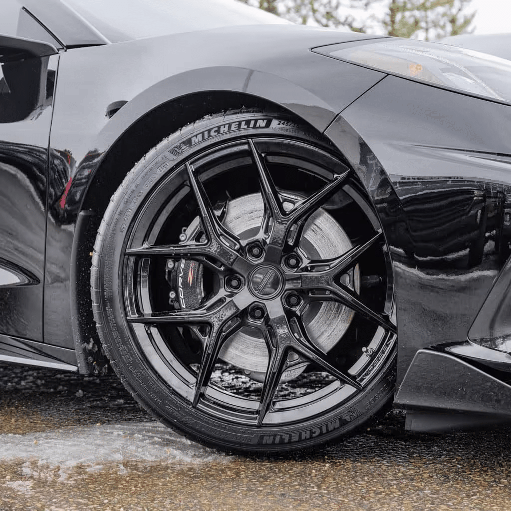 Close-up of a black sports car wheel featuring an intricate multi-spoke design, Michelin tire, and visible brake caliper.