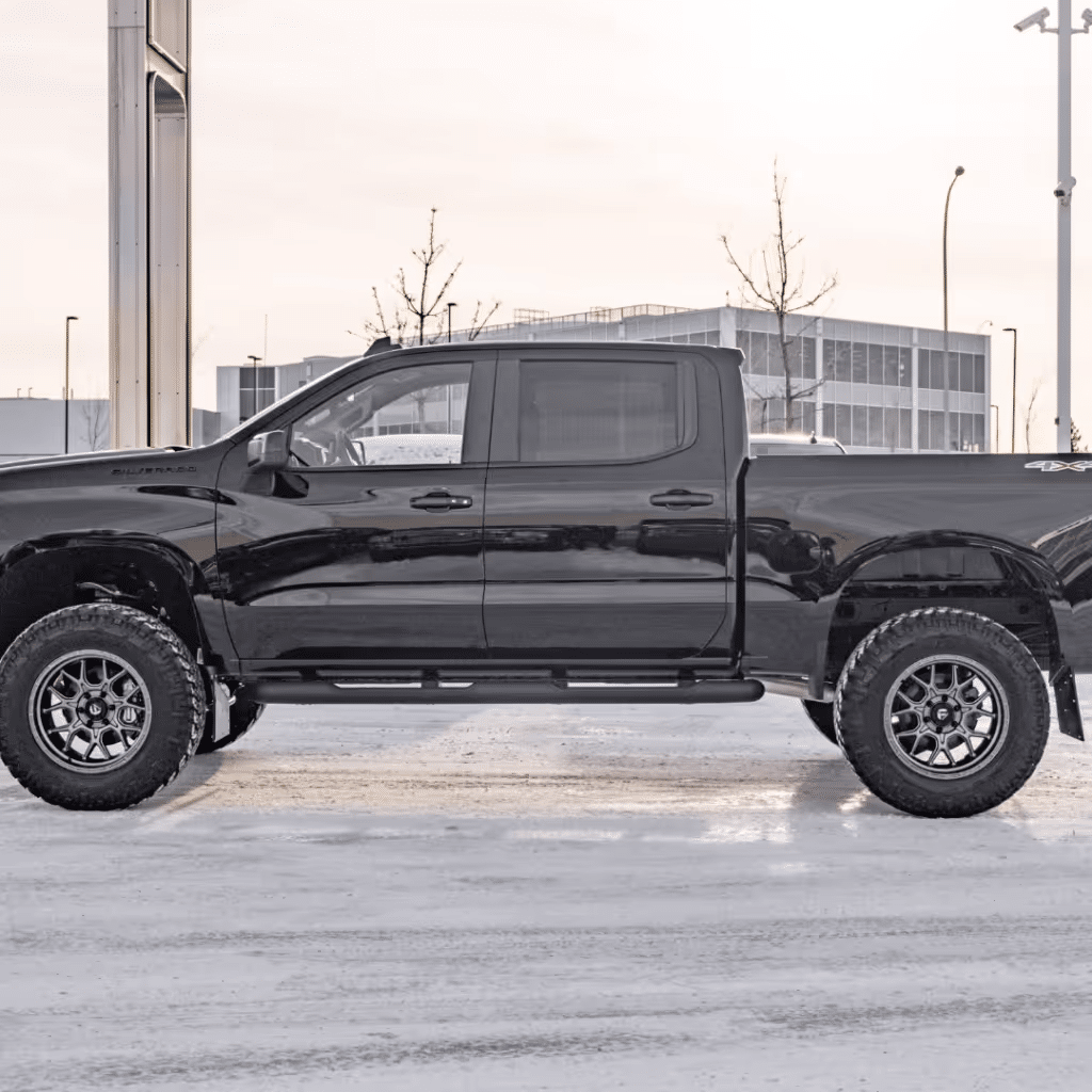 Black pickup truck with off-road tires parked in a snowy environment, showcasing an aggressive stance and modern design elements.