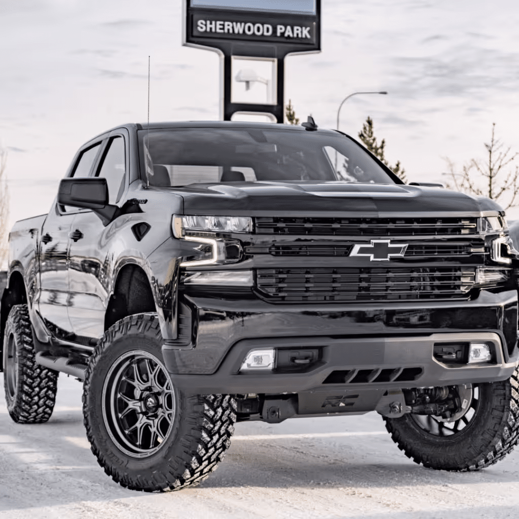 Black Chevrolet Silverado 1500 pickup truck with lifted suspension and rugged tires, parked in front of a Sherwood Park sign, showcasing its bold design and off-road capabilities.