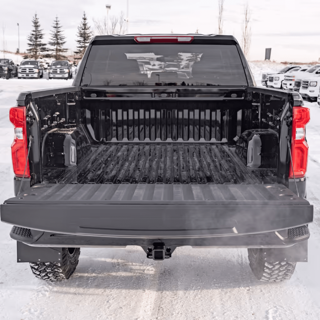Black pickup truck bed with a clear view from the rear, featuring a rugged, textured surface, spacious interior for cargo, and snow-covered ground in the background, showcasing winter conditions.
