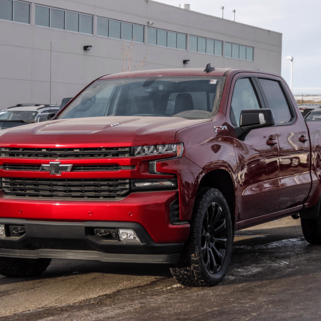Red Chevrolet Silverado Z71 truck parked in front of a dealership, showcasing its bold design and rugged features, including black wheels and an aggressive grille. Ideal for off-road adventures and heavy-duty tasks.