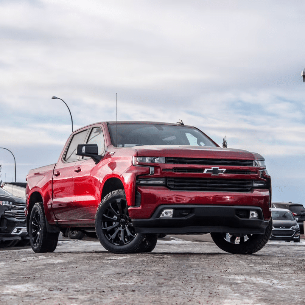 Red Chevrolet Silverado truck with black rims parked on a snowy lot, showcasing its rugged design and modern features.