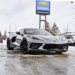 Silver Chevrolet Corvette C8 parked at Sherwood Park dealership, showcasing sleek design and stylish black wheels on a snowy surface with dealership signage in the background.