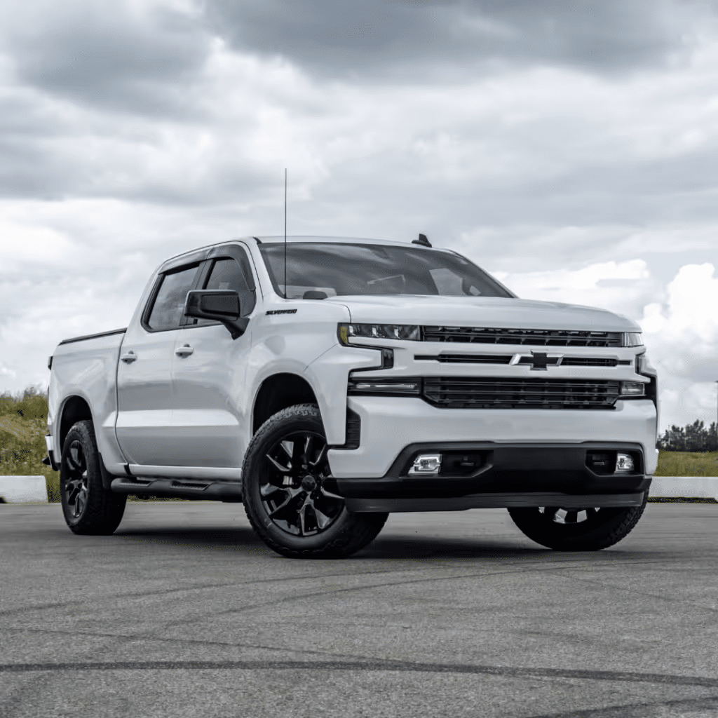 White Chevrolet Silverado pickup truck showcased on a cloudy day, featuring a bold front grille, modern design, and sleek black alloy wheels, set against an open outdoor environment.