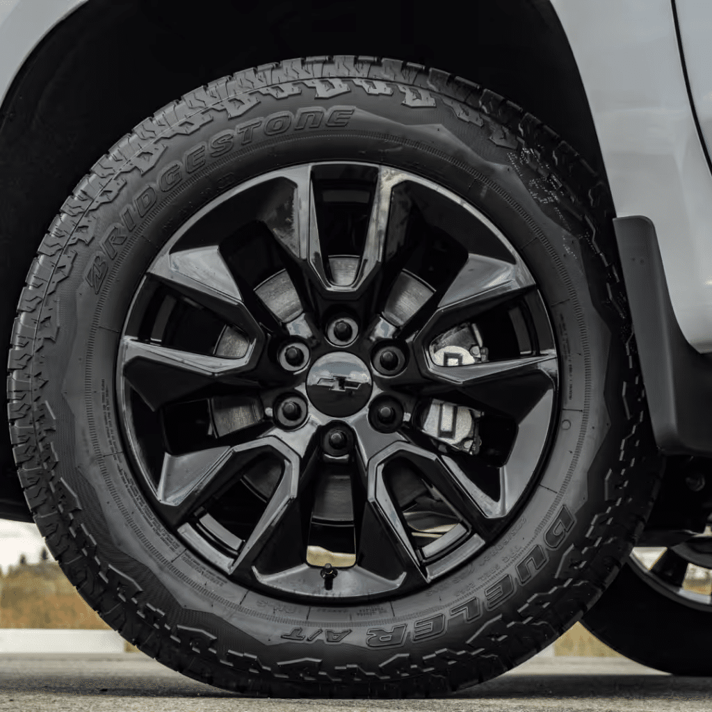 Close-up view of a black alloy wheel featuring a Chevrolet logo, mounted with a Bridgestone Dueler A/T tire, showcasing its rugged tread pattern, designed for off-road performance.