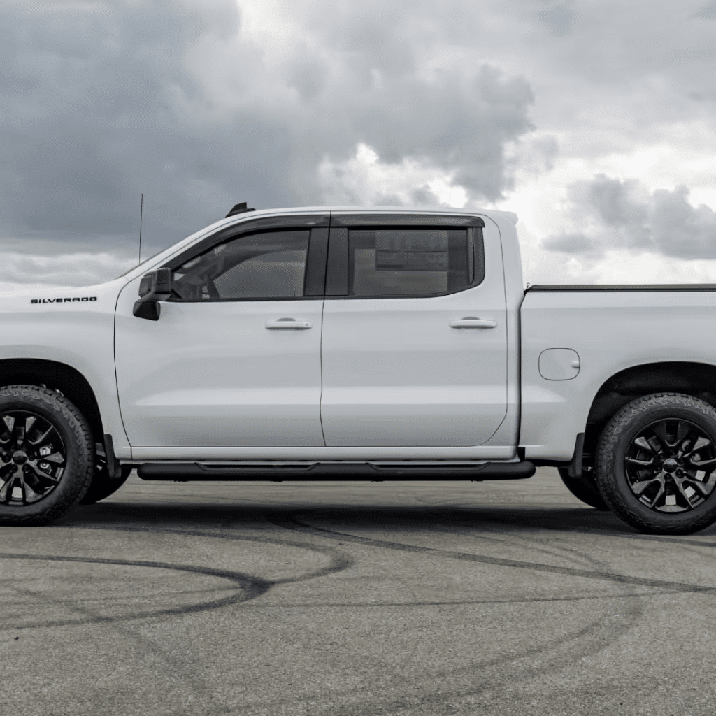 White Chevrolet Silverado pickup truck parked on a concrete surface, showcasing its sleek design, black wheels, and rugged profile against an overcast sky.