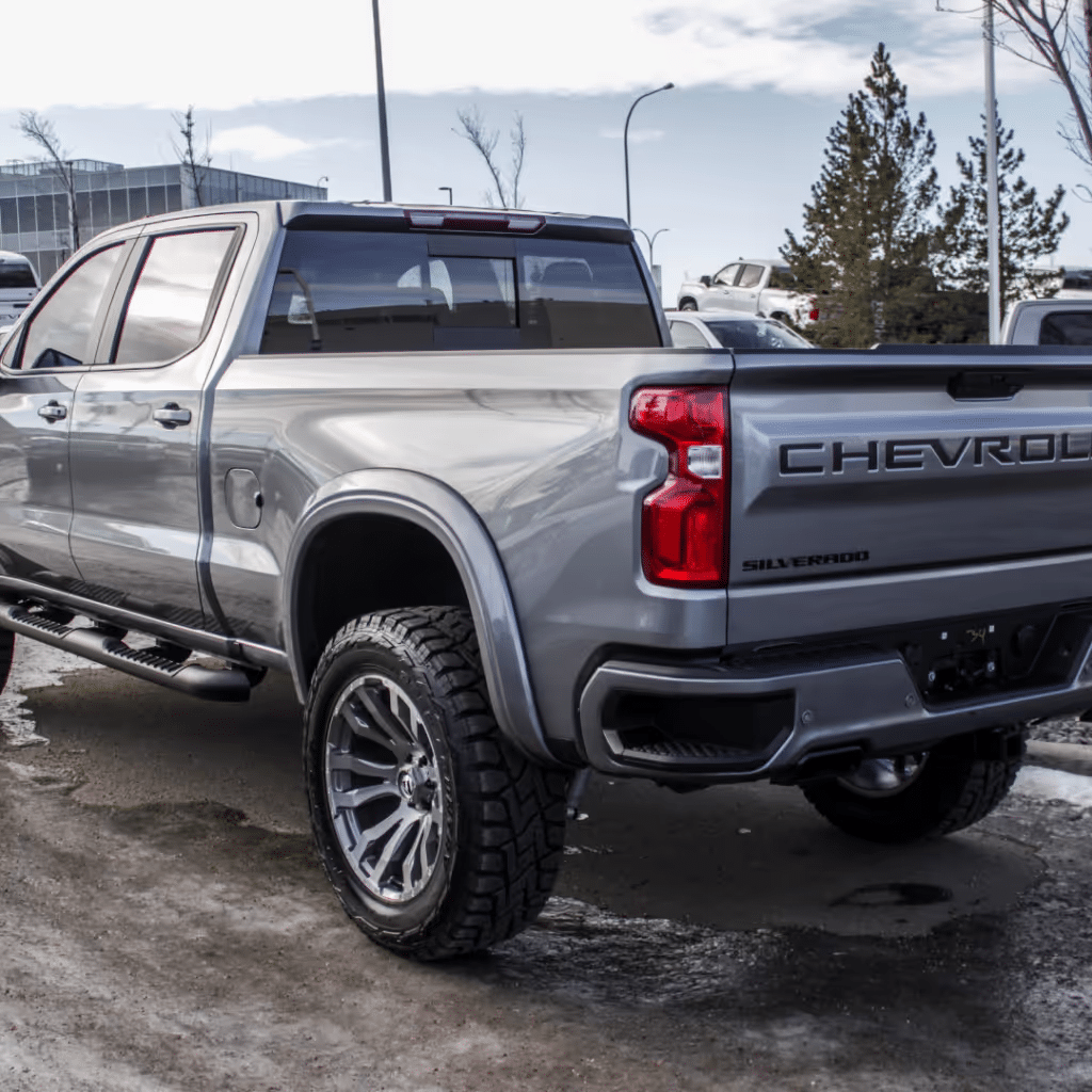 New Chevrolet Silverado truck in silver color, showcasing a sleek rear design with distinctive branding and modern alloy wheels, parked outdoors under a clear sky.