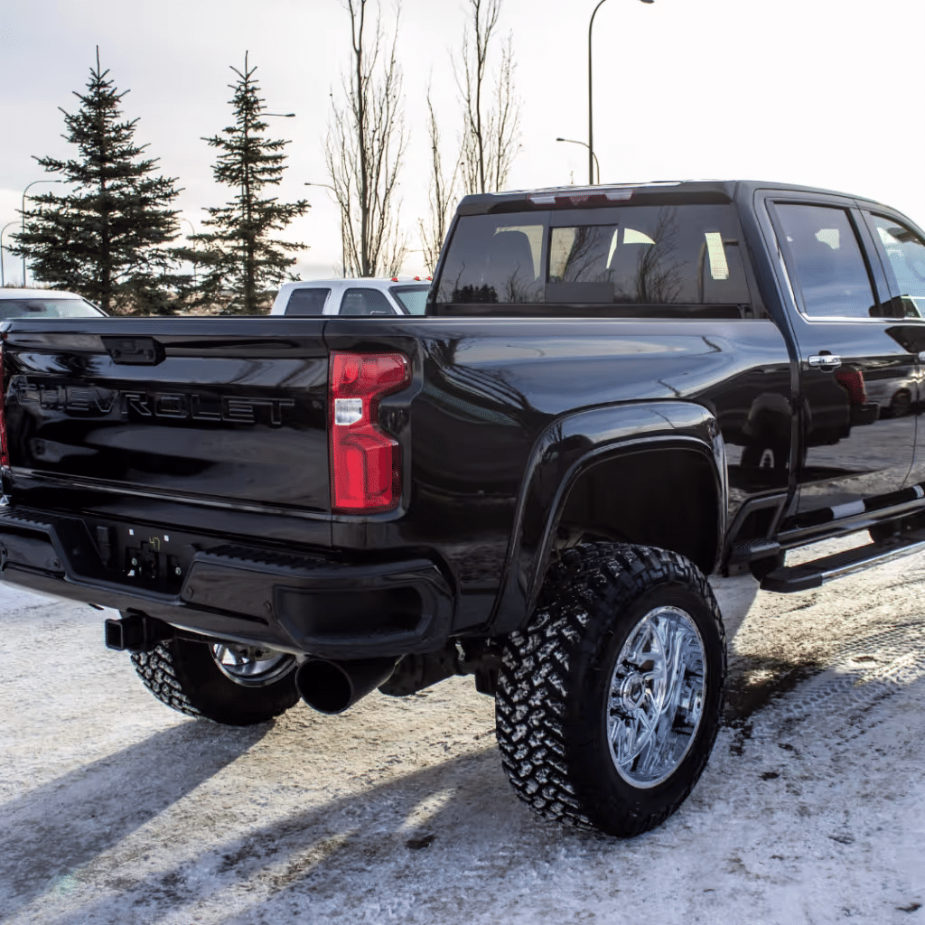 Black Chevrolet truck with a lifted suspension and chrome wheels parked on snow-covered ground, showcasing its rear features and modern design.