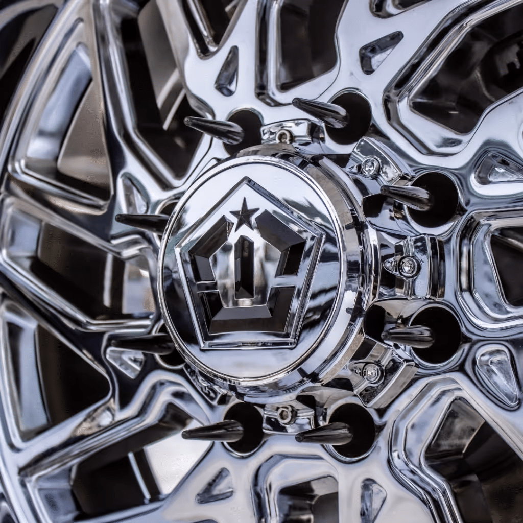Close-up of a shiny chrome alloy wheel with a detailed center cap featuring a star emblem and sharp protrusions, designed for enhanced aesthetics and performance.